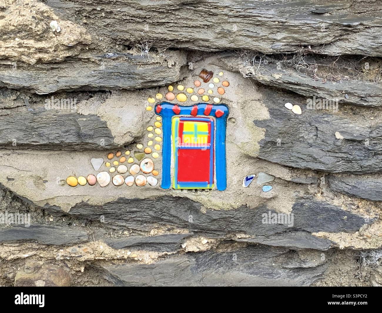 Colourful fairy door painted onto stone wall Stock Photo