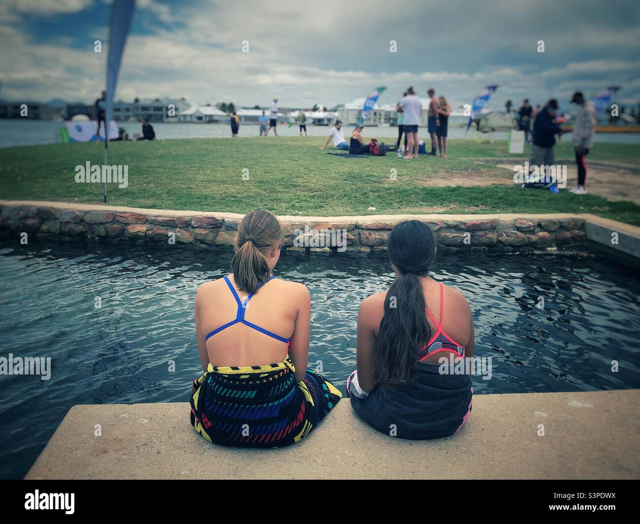 Two young ladies sitting and watching an open water swimming event in Marina Martinique, Jeffrey’s Bay, South Africa - Smartphone Captured Stock Image