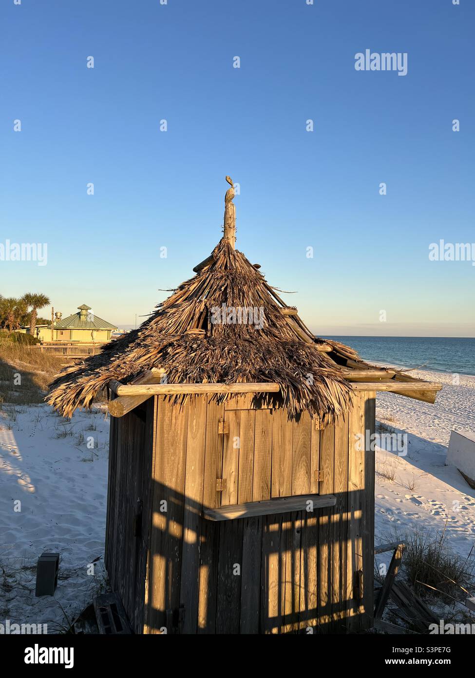 Sun setting shining on a tiki hut on white sand beach Stock Photo