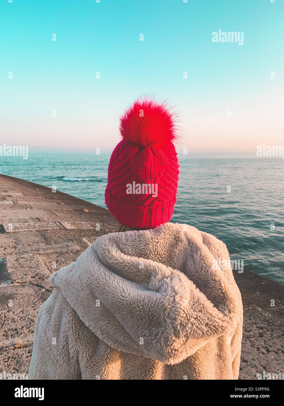 Woman looking out to sea wearing a red woollen bobble hat Stock Photo