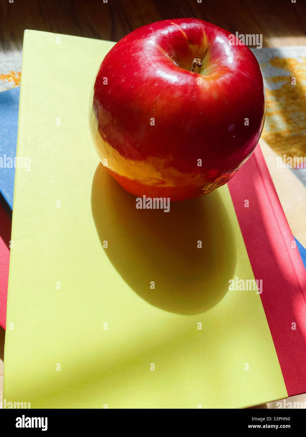 A shiny red apple sits atop elementary school textbooks, 2022, USA - Smartphone Captured Stock Image