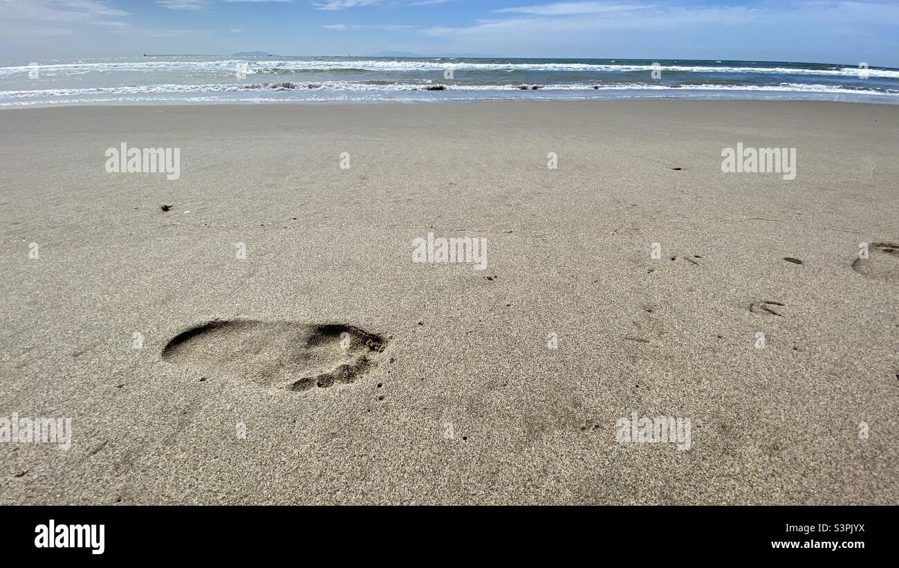 Footprint on sandy beach with waves breaking on Pacific Ocean and distant islands visible in background, California - Smartphone Captured Stock Image