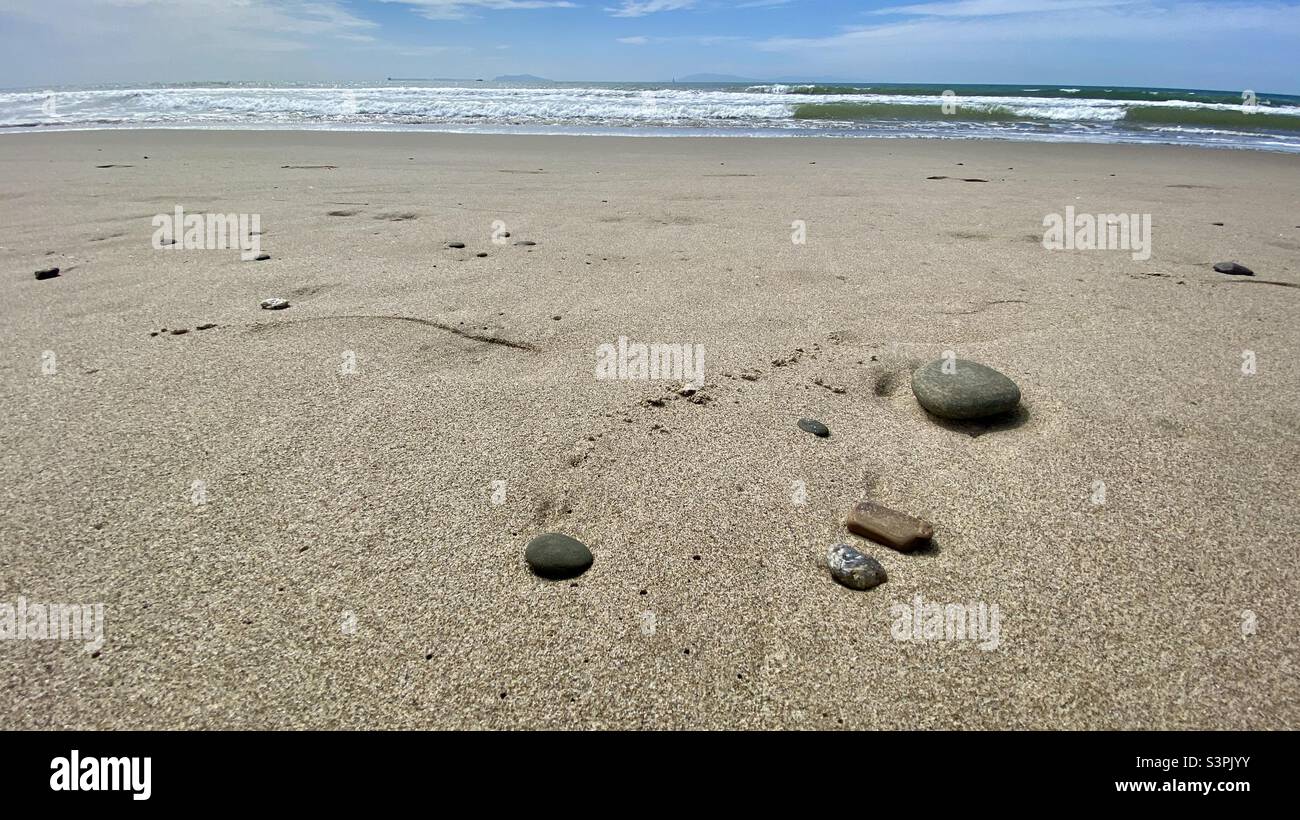 Small pebbles on pristine sandy beach with waves breaking on Pacific Ocean and distant islands visible in background, California Stock Photo