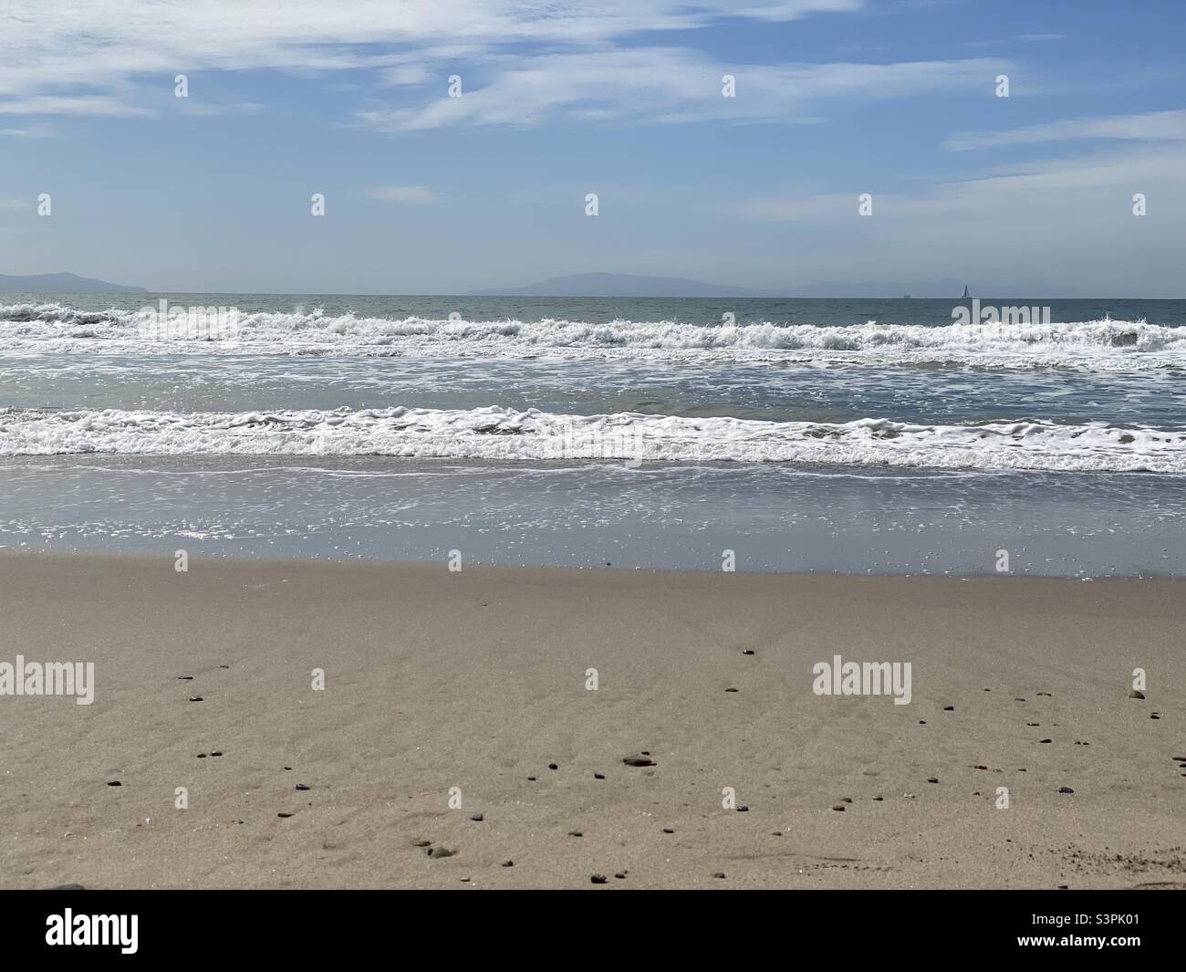 Sun glints off gently breaking Pacific Ocean waves at Ventura Beach, California. Sailboat and islands in distance - Smartphone Captured Stock Image