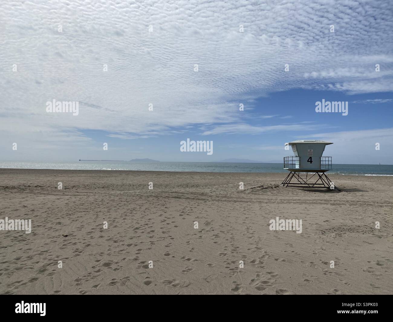 VENTURA BEACH, CA, MAR 2021: lifeguard hut on sandy beach with footprints and tire tracks. Pacific Ocean and islands in distance. Cloudy sky - Smartphone Captured Stock Image