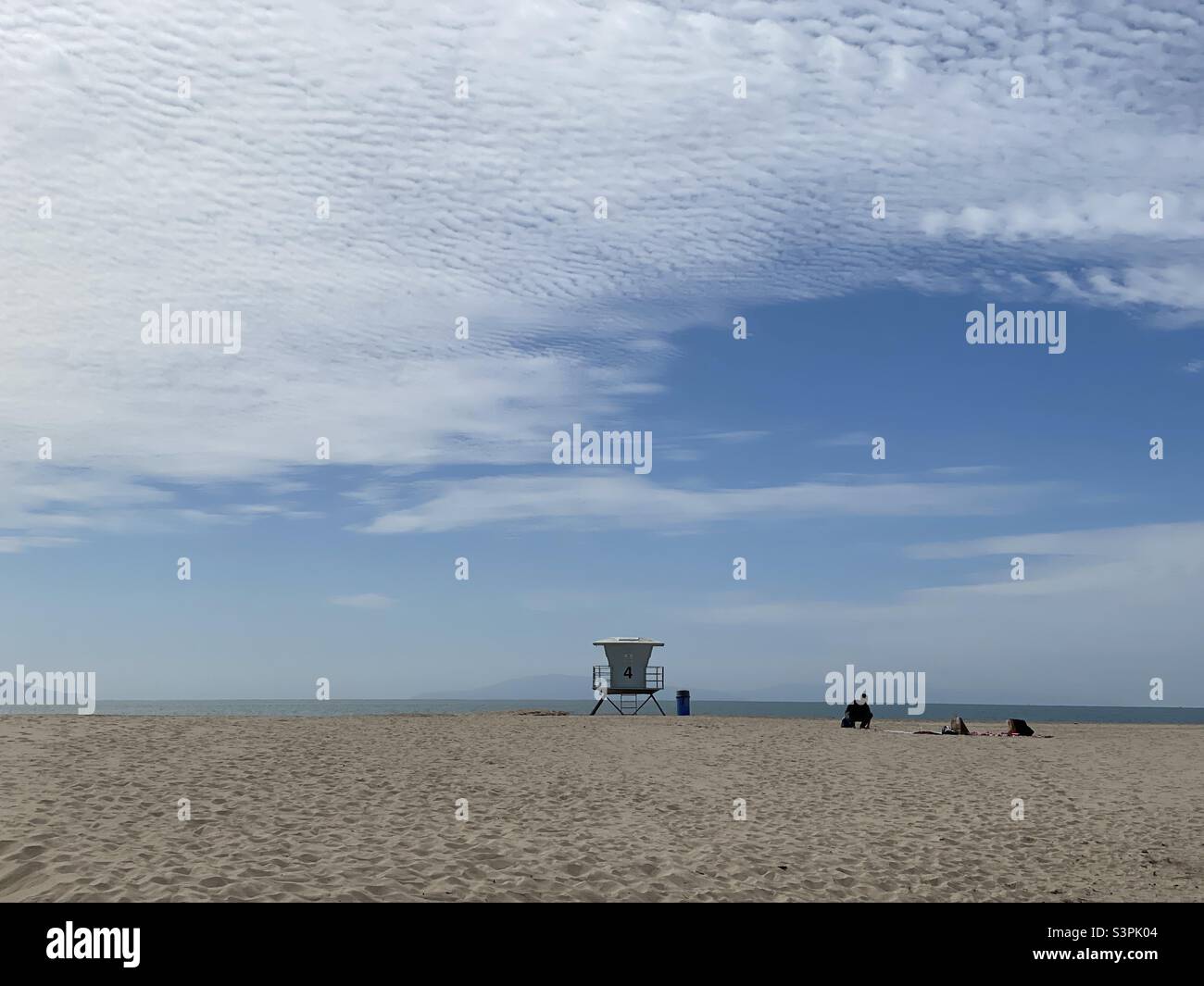 VENTURA BEACH, CA, MAR 2021: wide view with centered life guard hut on the beach and anonymous silhouetted person nearby. Clouds and blue sky overhead - Smartphone Captured Stock Image
