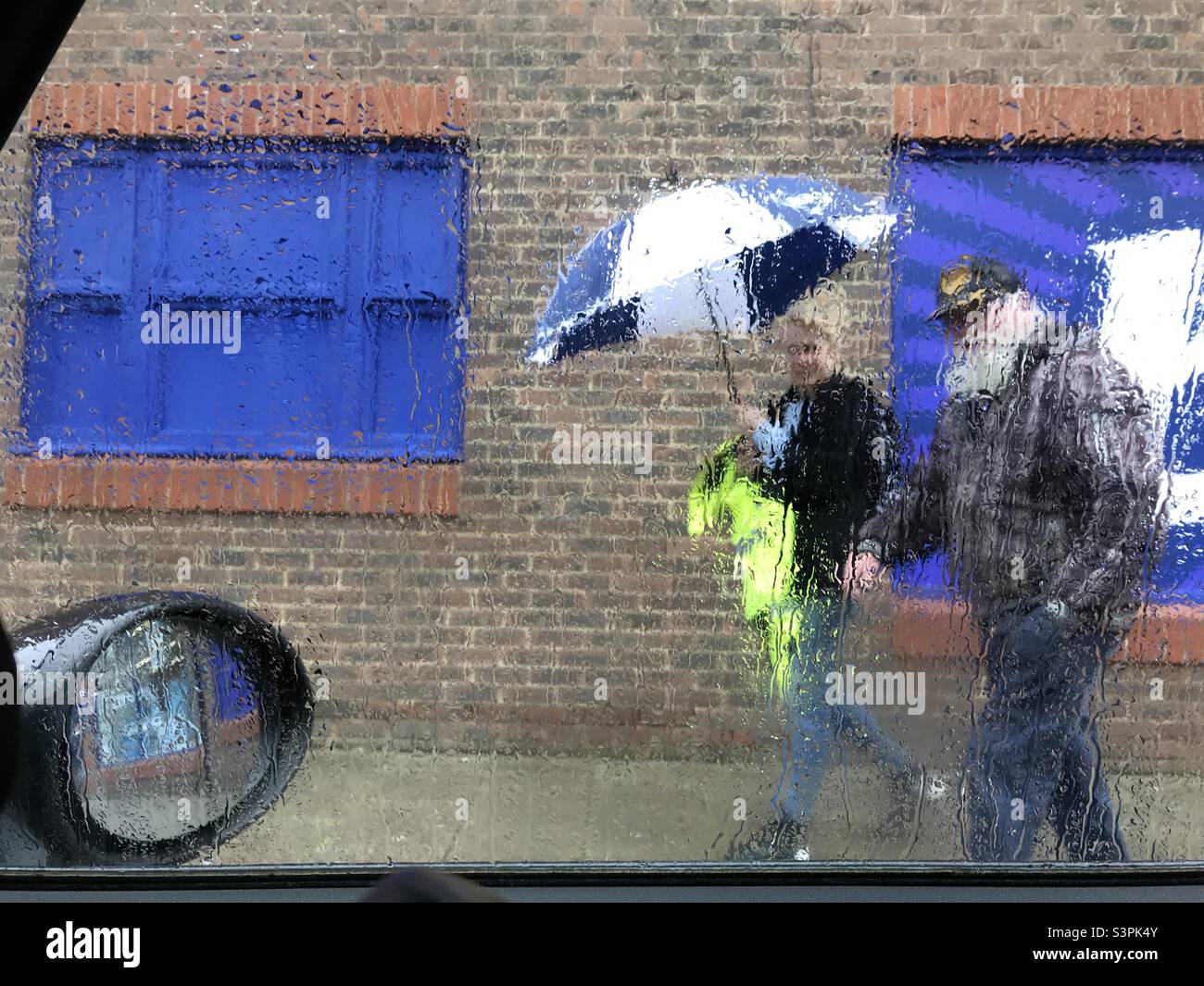 Rainy weather umbrella street scene pedestrians walking through car window dripping wet Stock Photo