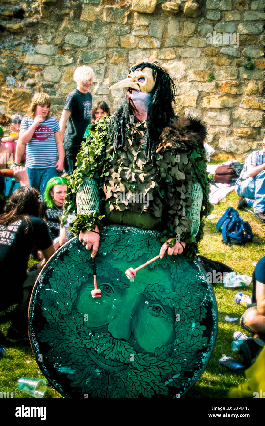 A bogey wearing green and a beak mask, plays a large drum painted with the face of the green man Traditional Hastings Jack in the Green festivities. UK, May 2008 - Smartphone Captured Stock Image