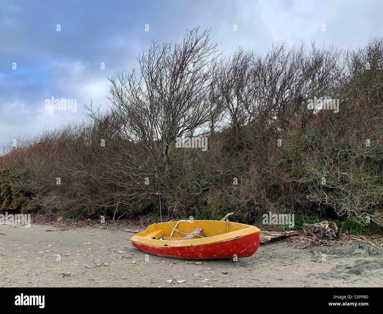 Red and yellow dinghy boat washed up onto beach Stock Photo