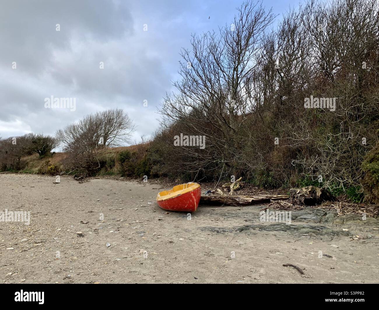 Small red dinghy boat washed up on beach Stock Photo