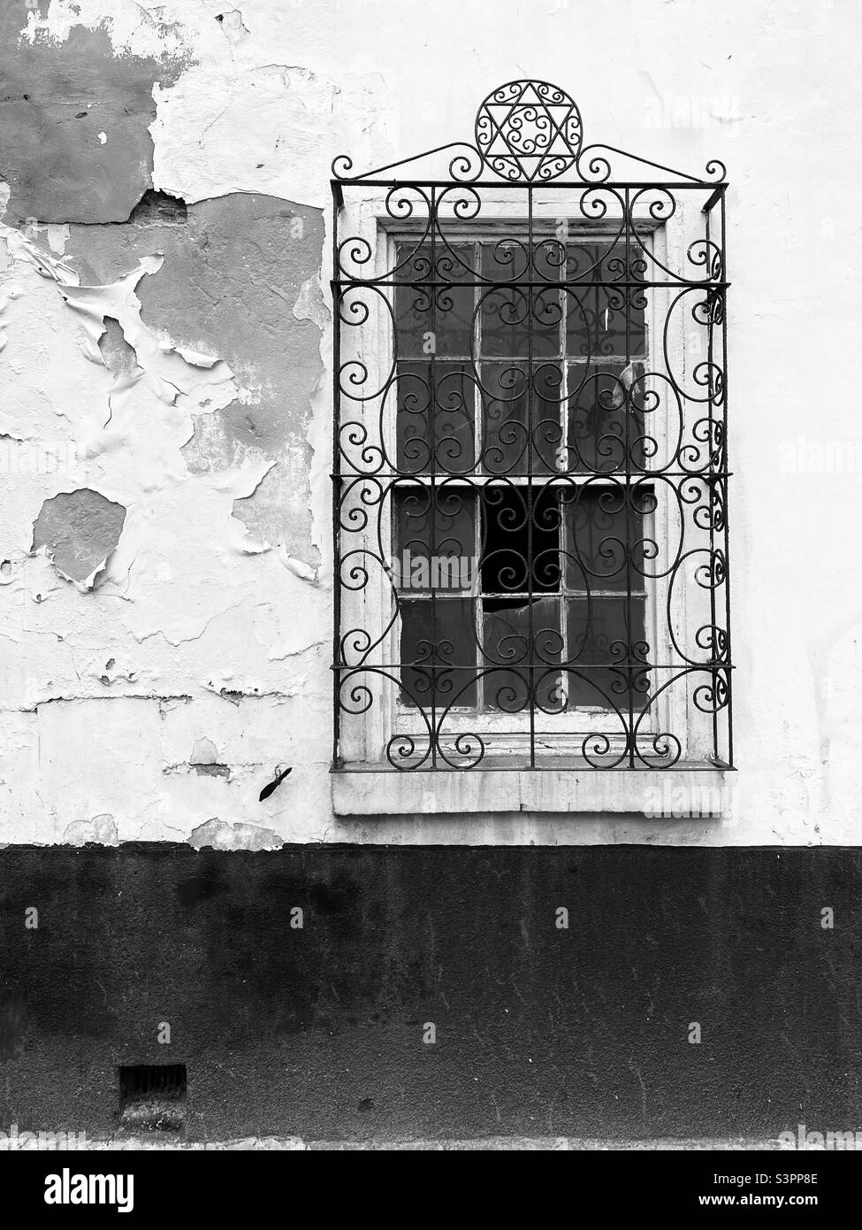 Window with ornate metal grill on an old building with peeling paint Stock Photo