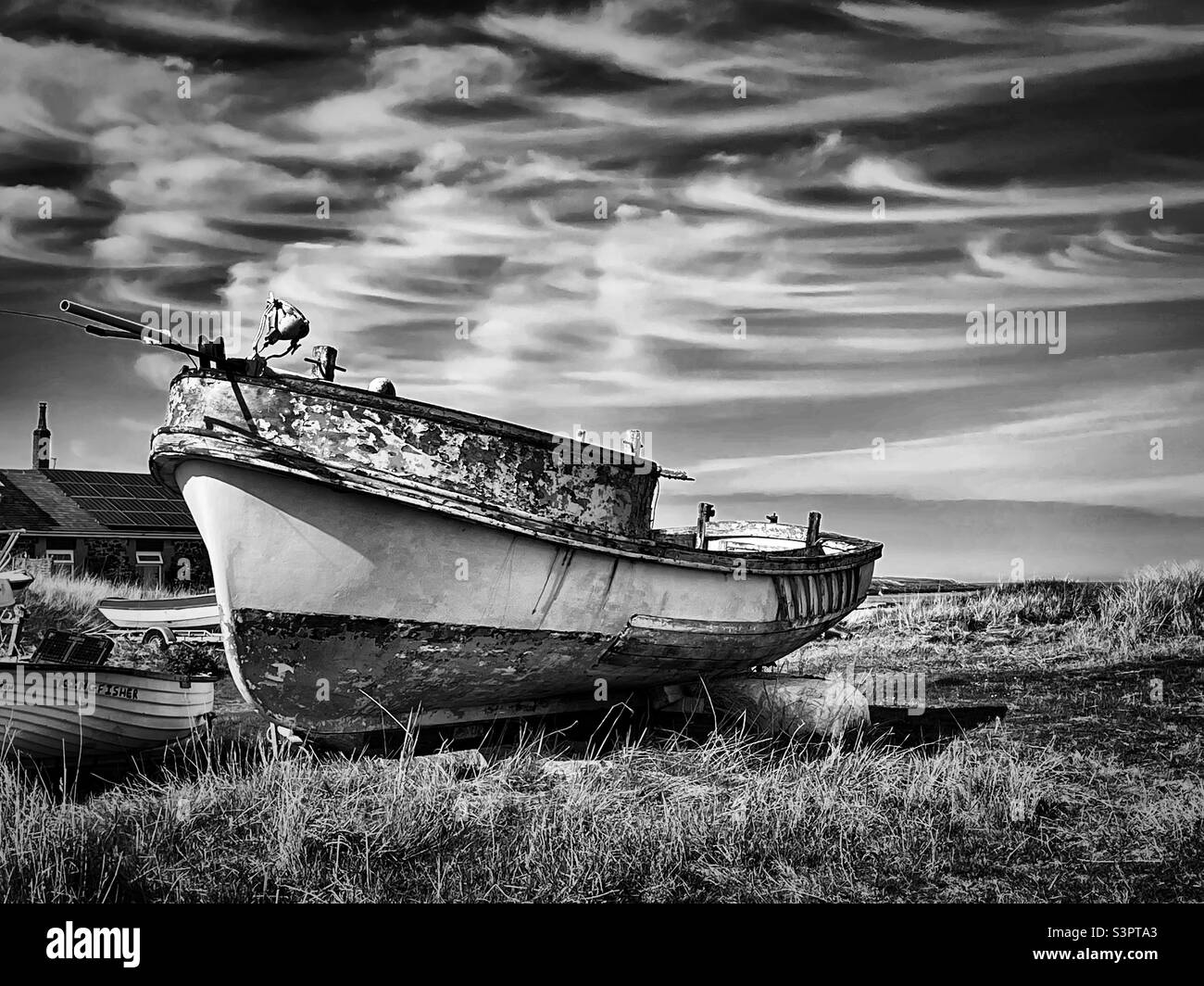 ‘Boat Graveyard’ an old boat comes to its final resting place next to the sea it sailed many times before (Black & White) Stock Photo
