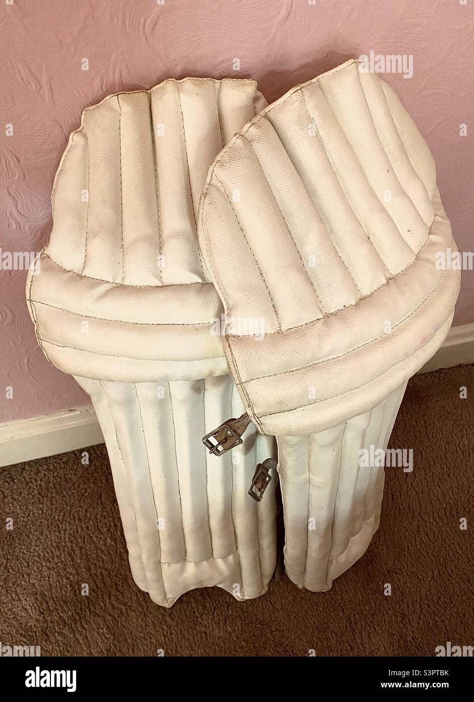 Cricket (batting) pads awaiting putting into the cricket bag alongside other equipment for the game. These leg guards are essential protection for a cricketer alongside other equipment. Stock Photo