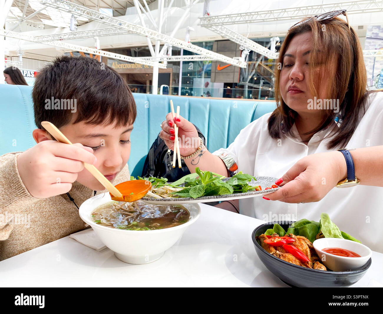 Mother and son sharing Vietnamese food in a food court. - Smartphone Captured Stock Image