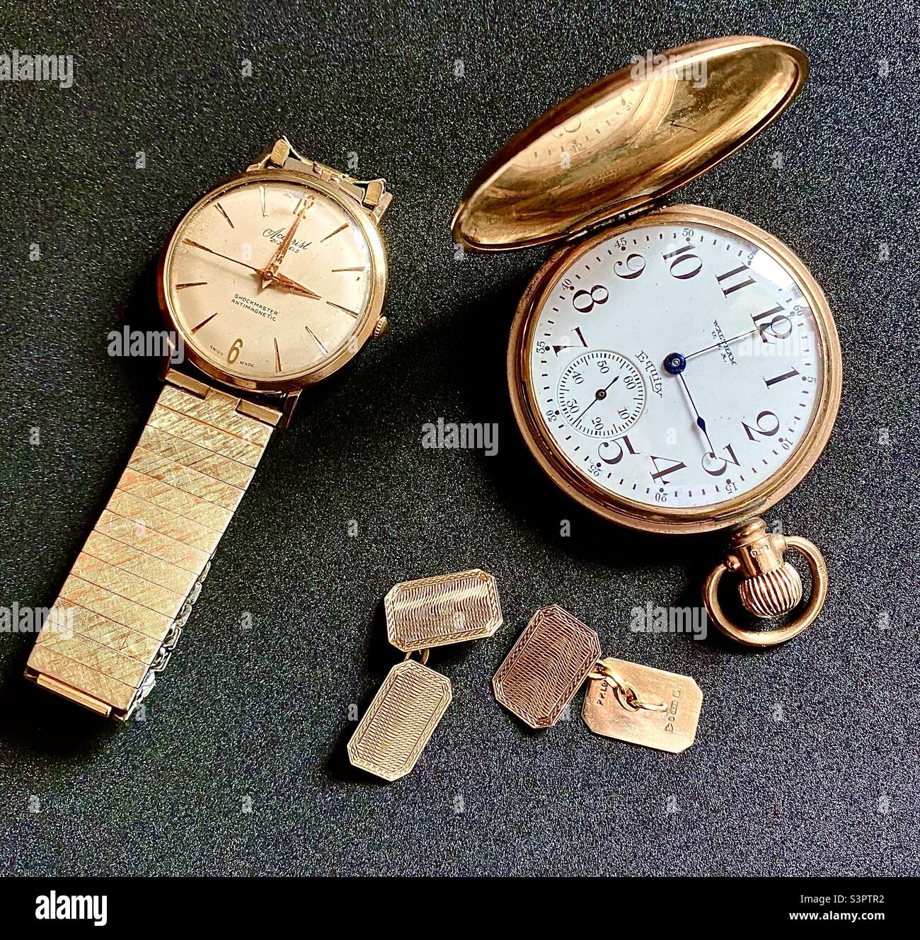 Black background showing gentleman’s gold accessories: a vintage Waltham (USA) Equity gold pocket watch, an Accurist Shockmaster Anti-magnetic gold wrist watch and a pair of vintage gold cuff links. Stock Photo