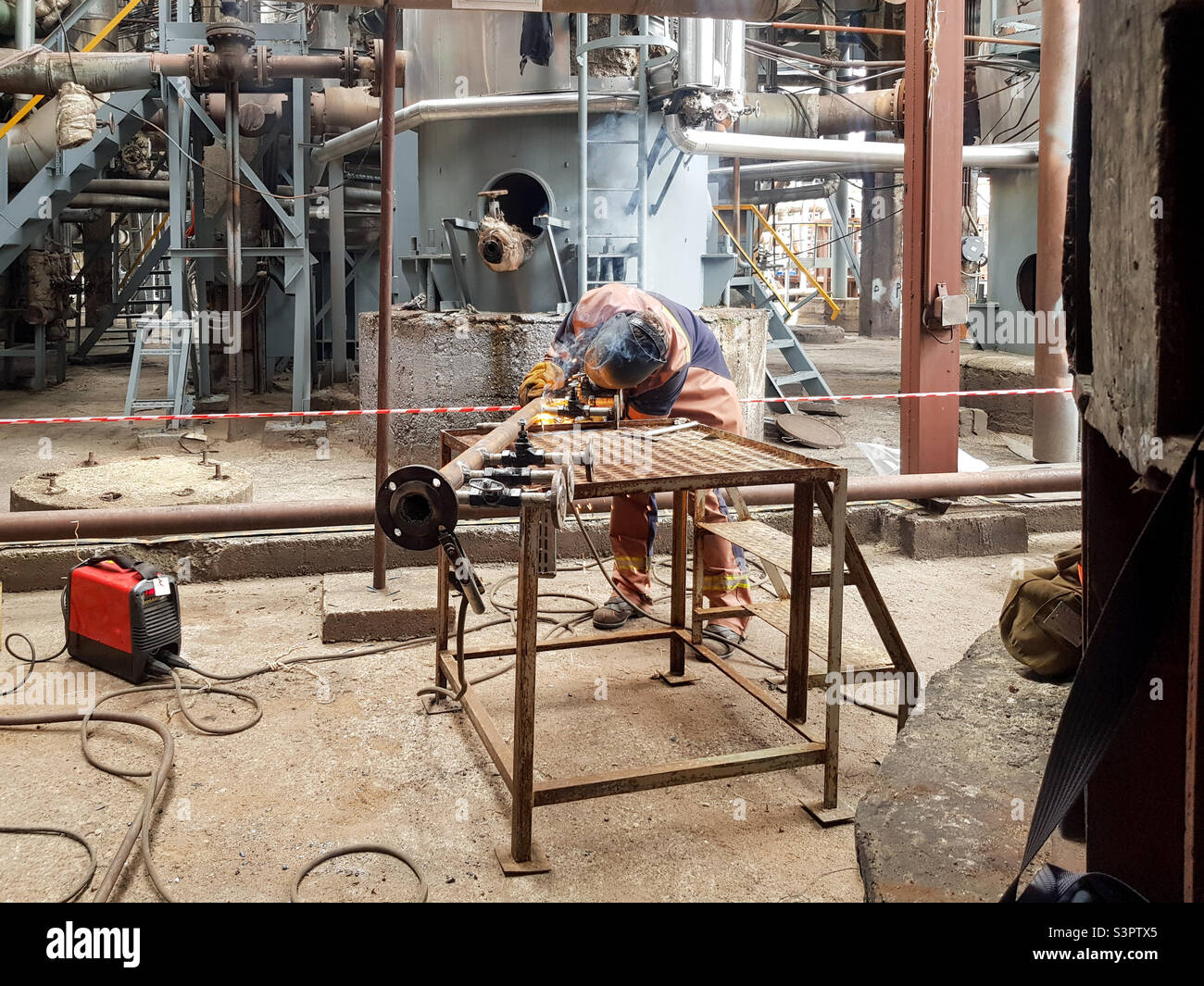 A man welder is engaged in welding metal on the pipeline and flanges - Smartphone Captured Stock Image