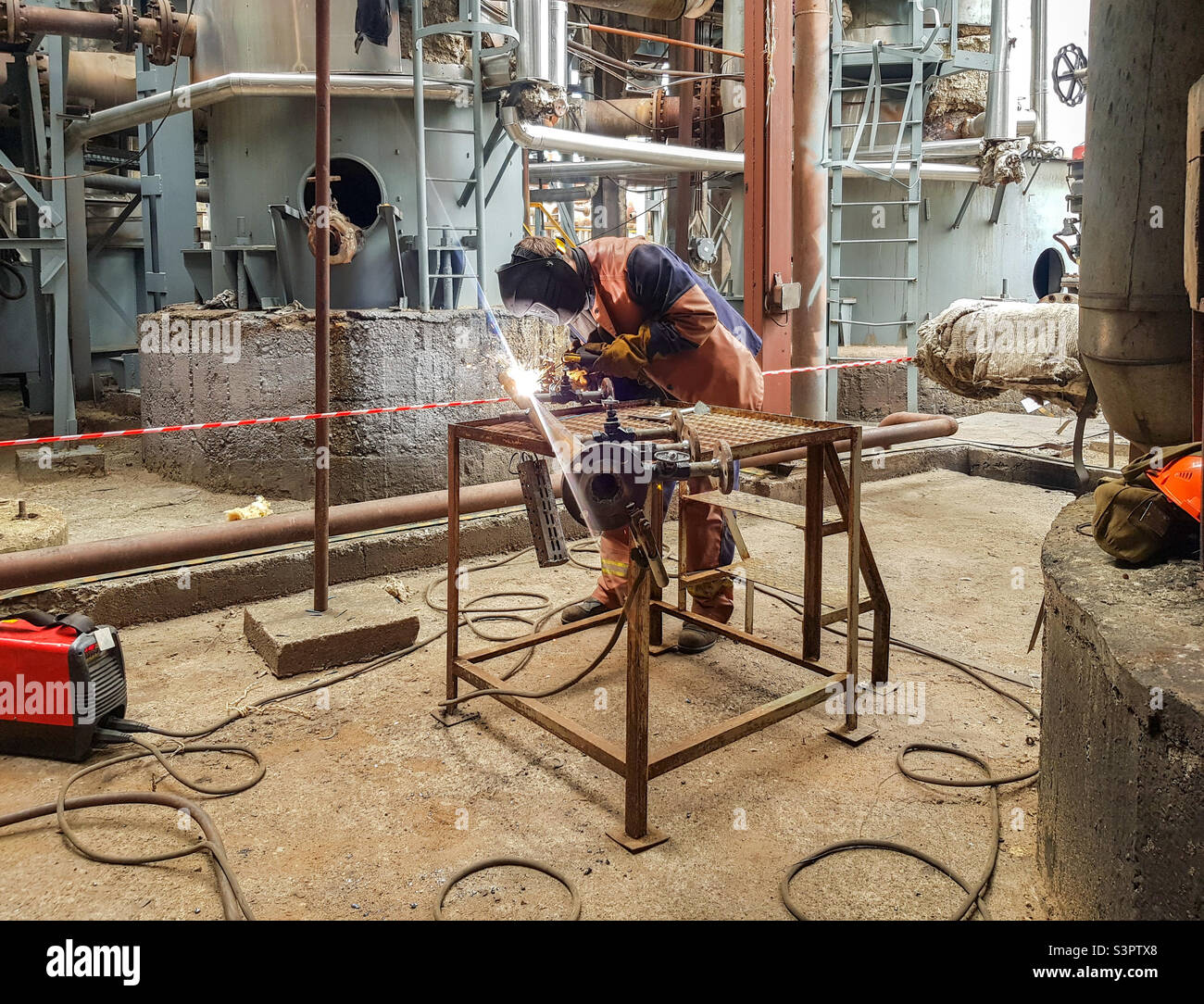 A man welder is engaged in welding metal on the pipeline and flanges - Smartphone Captured Stock Image