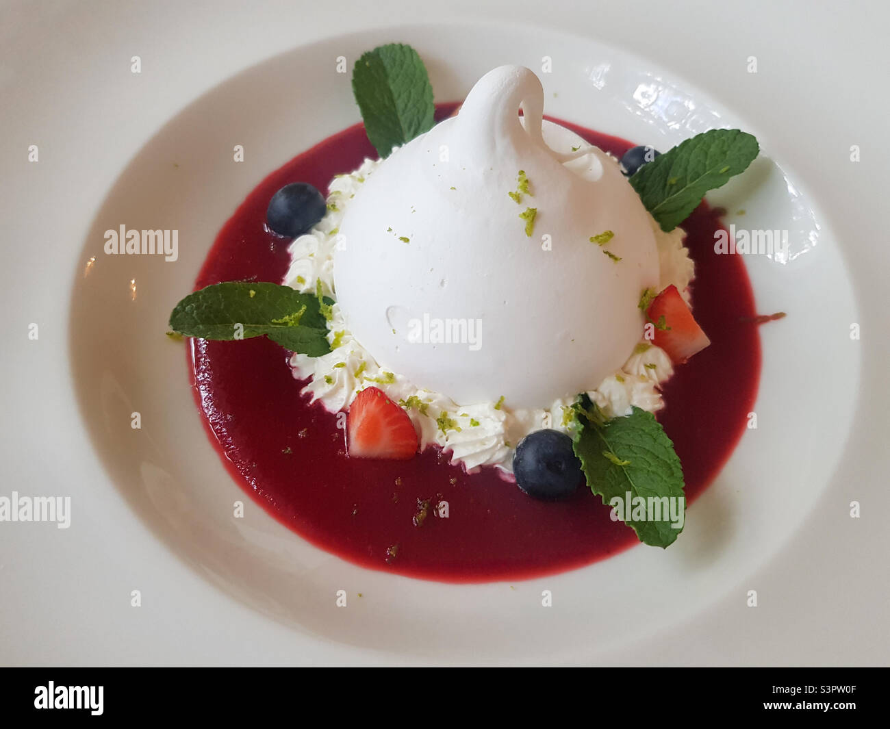 Delicious Pavlova dessert on a white plate close-up.  Pavlova dessert is an airy soft cloud and an amazing taste combination of berries, butter cream and protein dough - Smartphone Captured Stock Image