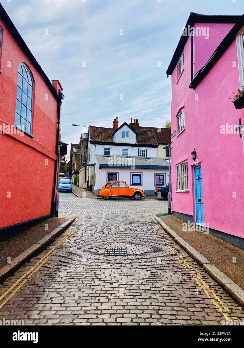 Colour Fix! Vivid orange Citroen 2CV parked on a street, pink houses, bright blue door, double yellow lines. Ten Bell Lane, Norwich, UK Stock Photo
