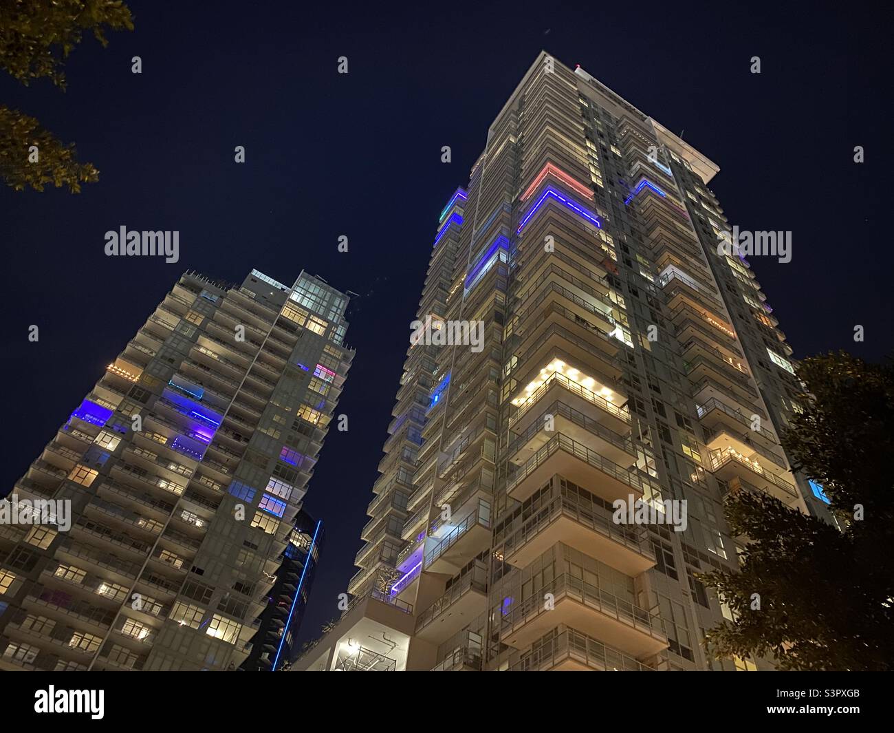 Looking up at two high-rise towers of apartments in Downtown Los Angeles, lit up with different colors at night - Smartphone Captured Stock Image
