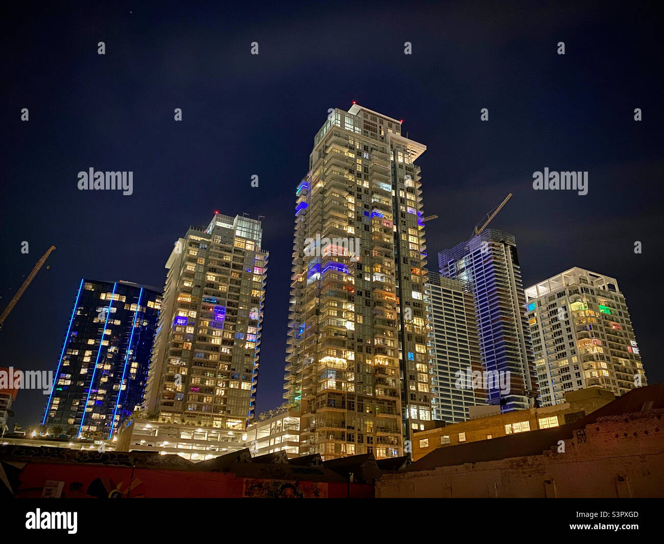 Group of high-rise towers of apartments in Downtown Los Angeles, some under construction, lit up with different colors at night - Smartphone Captured Stock Image