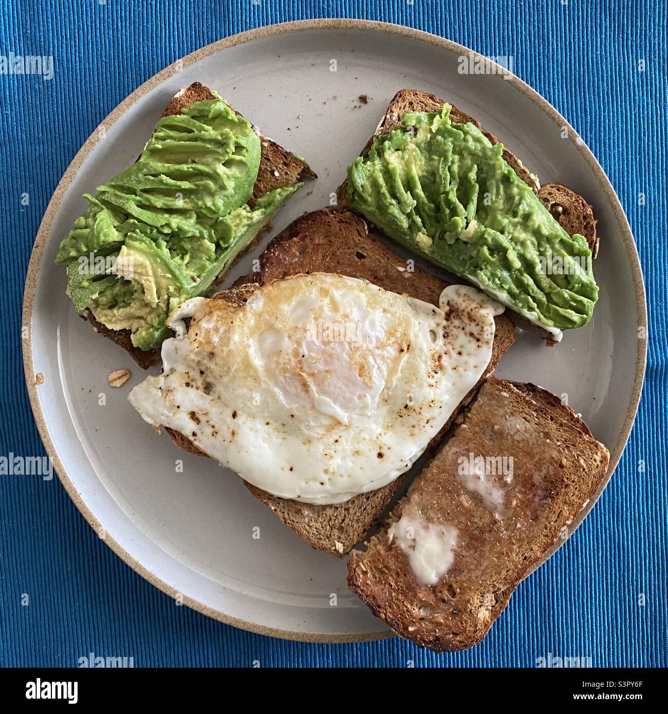 Breakfast with whole grain avocado toast and a fried egg on a grey ceramic plate - Smartphone Captured Stock Image