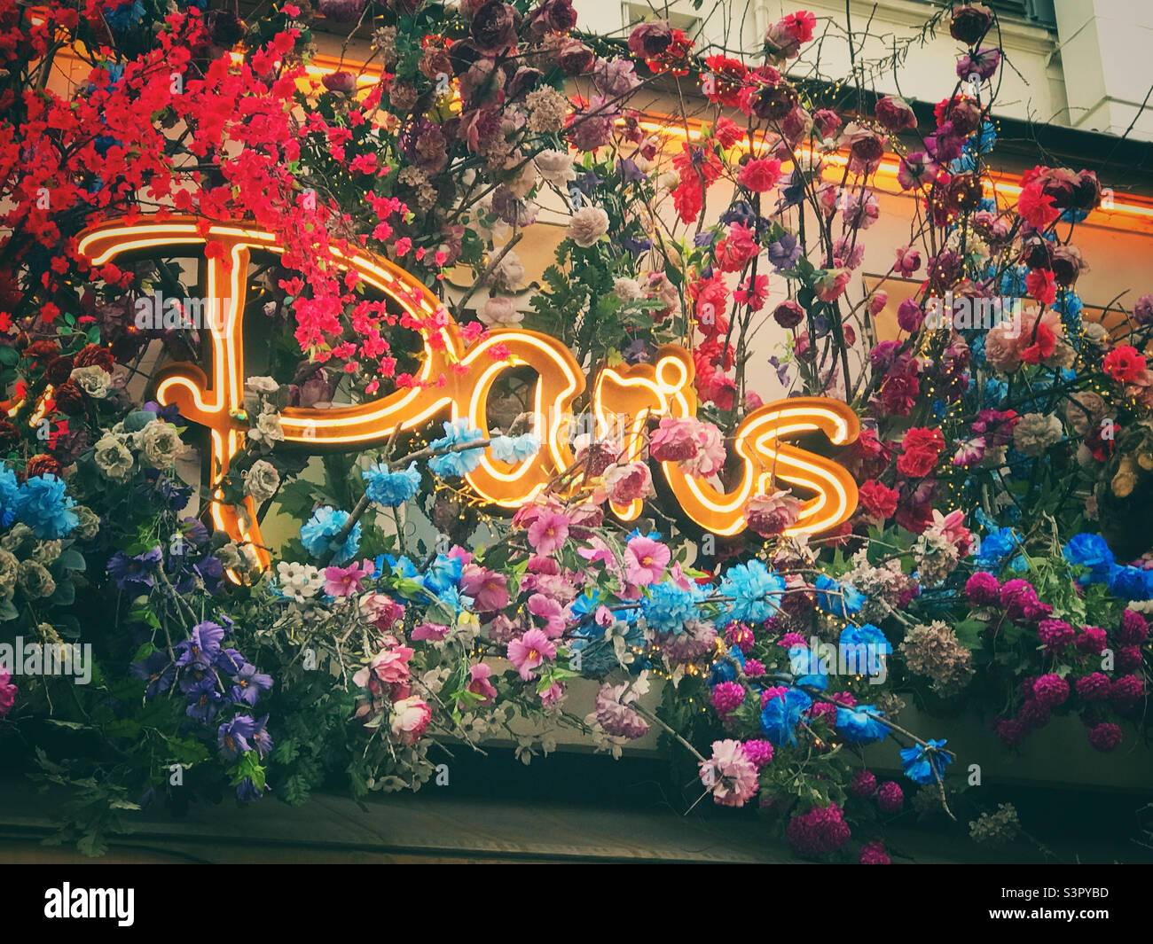 A neon Paris sign surrounded by flowers above a Parisian restaurant Stock Photo