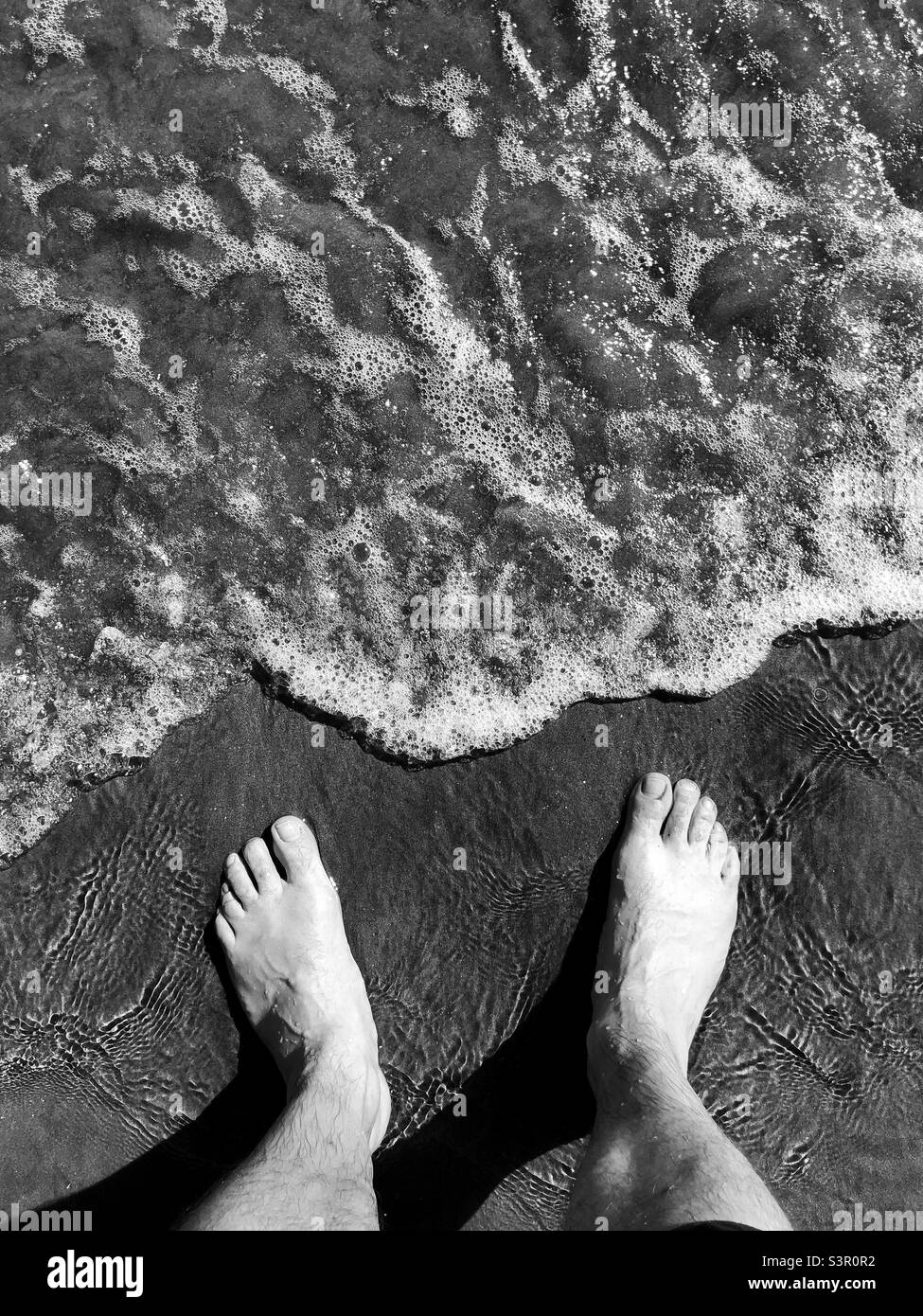 Black and white picture of feet standing at the waters edge Stock Photo