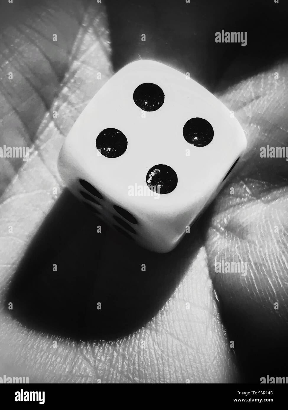 A black and white photograph of a single die showing the number four (4) Stock Photo