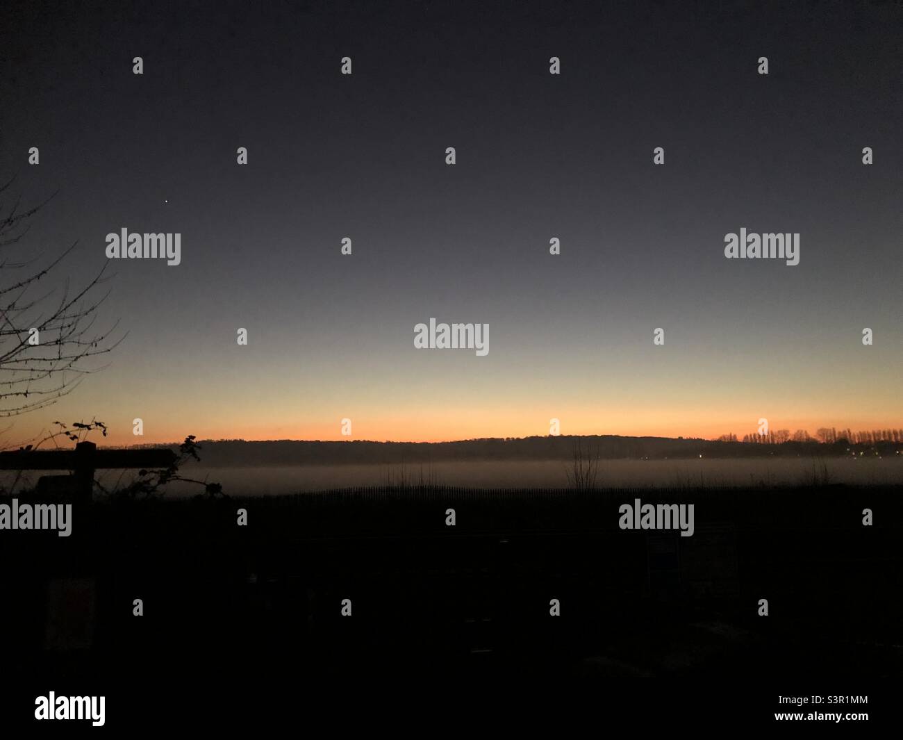 Winter sunset at Port Meadow, Oxford, England, with a band of orange sky and mysterious fog rising from ground level and the first stars showing. Stock Photo