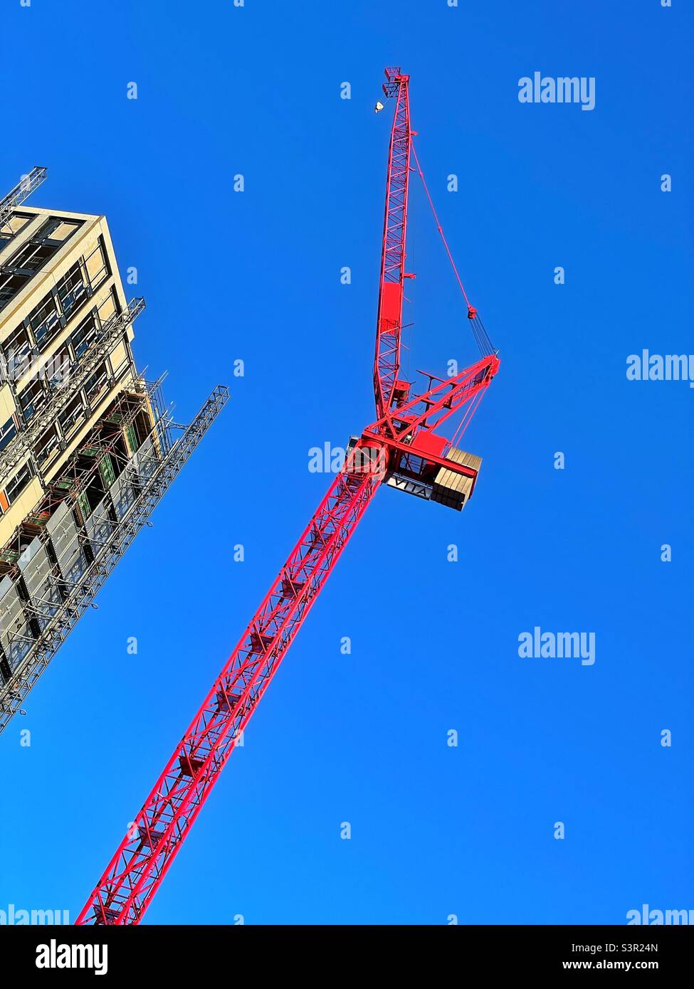 Large red crane at a construction site against a clear blue sky. - Smartphone Captured Stock Image