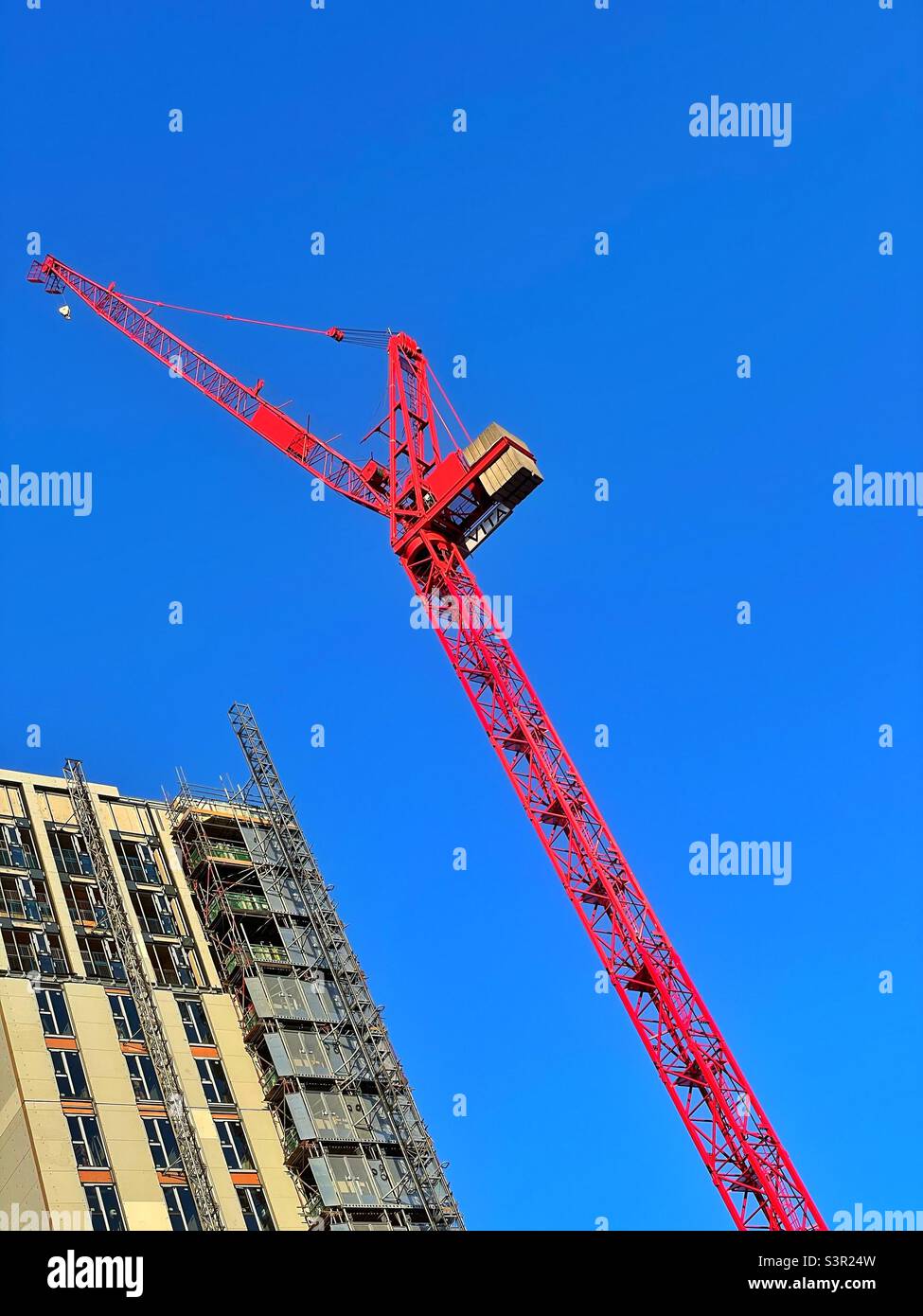 Large red crane against a blue sky, during construction of a tall building in a city. Stock Photo