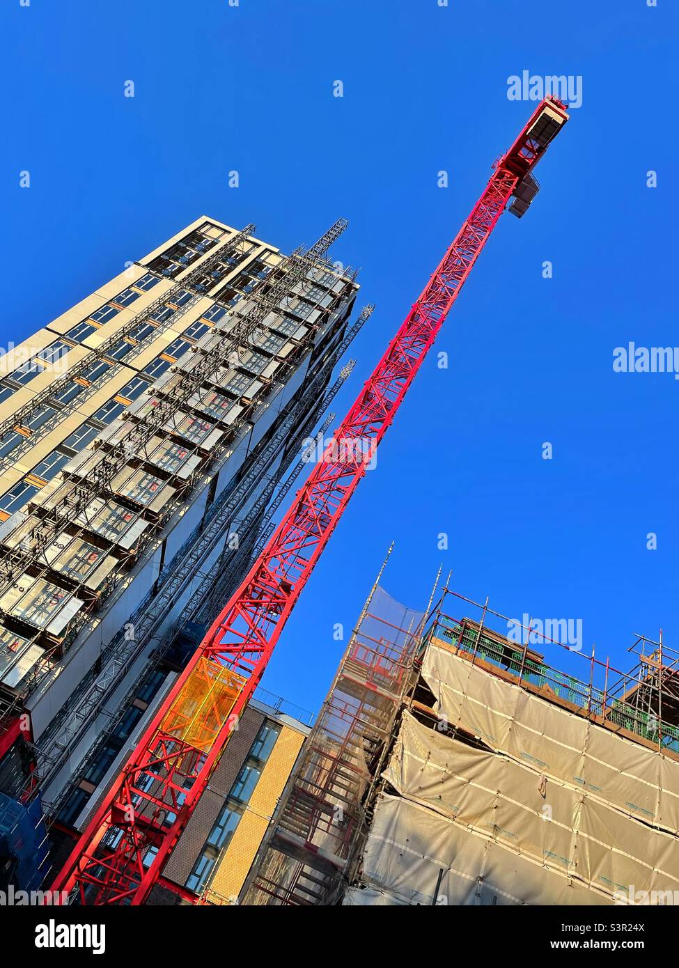 Construction of a tall building in a city with a big red crane against a blue sky. - Smartphone Captured Stock Image
