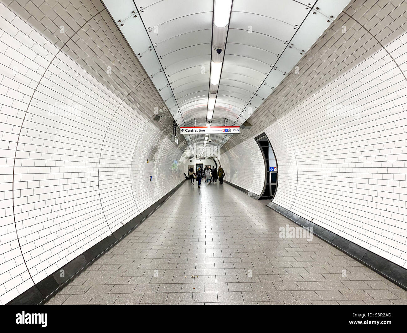 View along a long white tunnel at Tottenham Court Road London Underground station heading towards the Central Line trains. - Smartphone Captured Stock Image