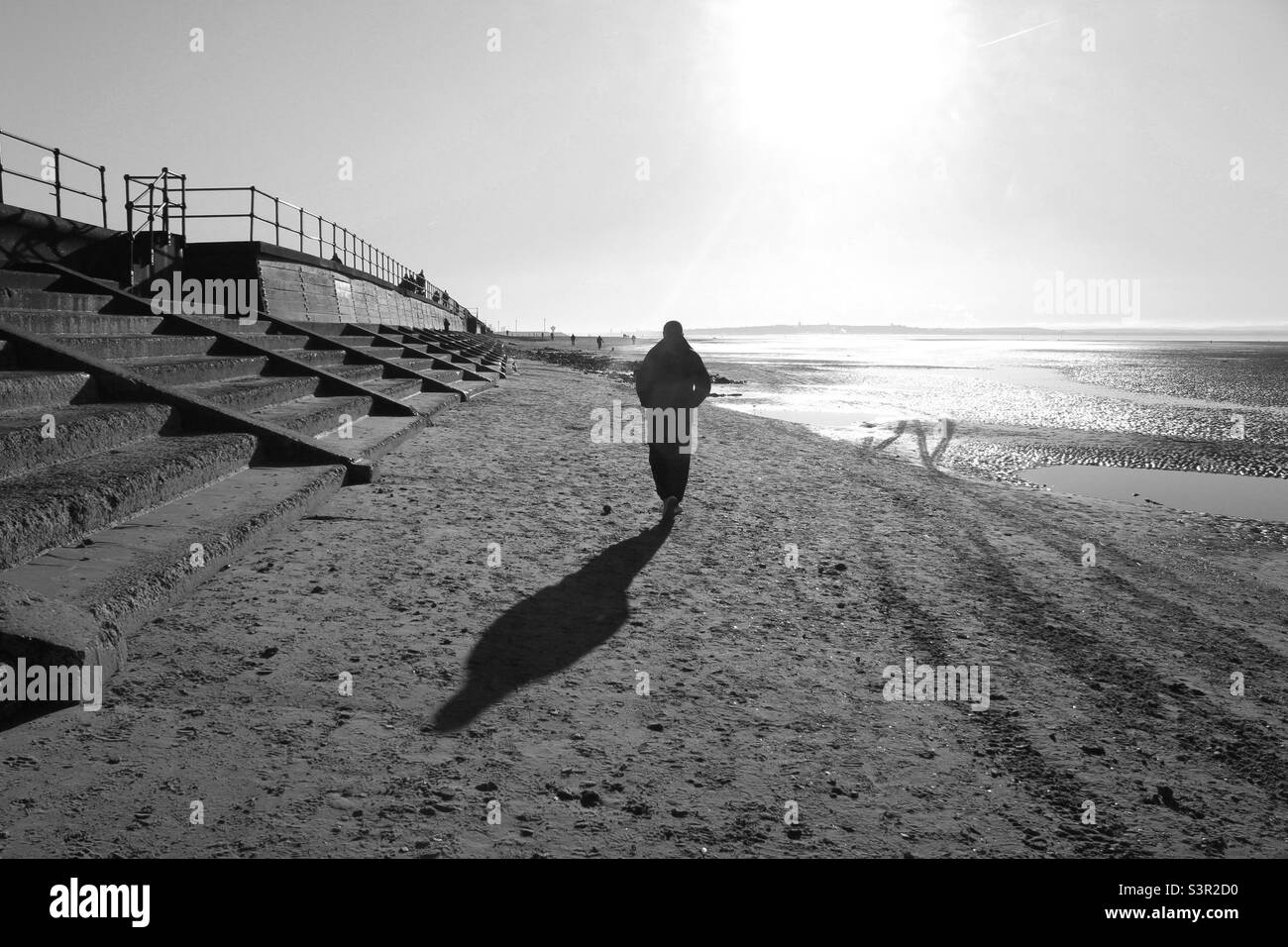 Man walking along the beach under the sunrise. Photo was taken at Crosby beach in Liverpool, Merseyside. - Smartphone Captured Stock Image