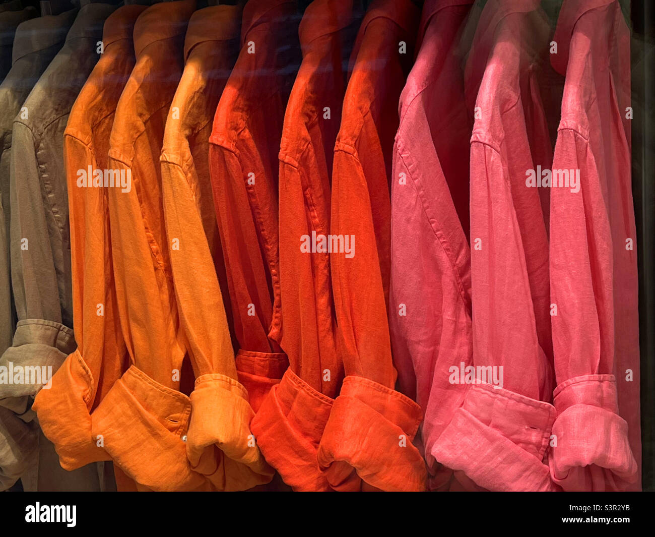 Orange, red and fuchsia shirts in a shop window. Stock Photo