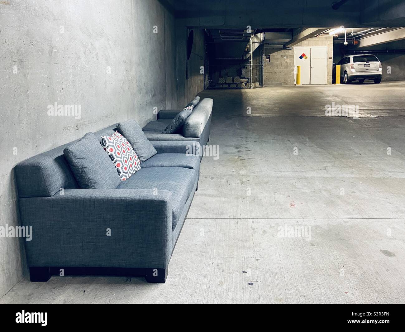 Two grey couches with cushions, left on cement floor at the side of a a