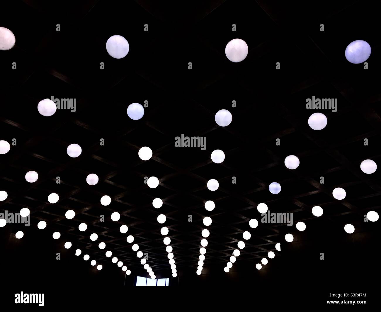 Strings of bright ceiling lights, parallel  rows but they appear to be radiating from this angle. Looking up. Monochrome. High contrast. Design. Pattern. Design - Smartphone Captured Stock Image