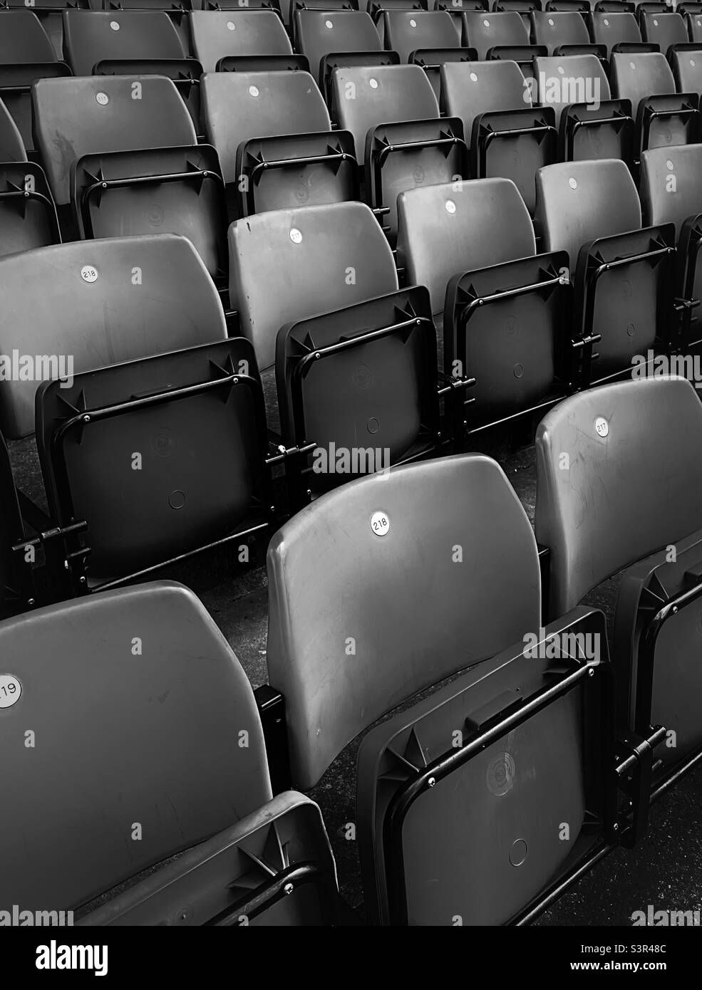 ‘Seats Available’ empty red seats inside a football stadium before the supporters fill them up on match day (Black & White) Stock Photo