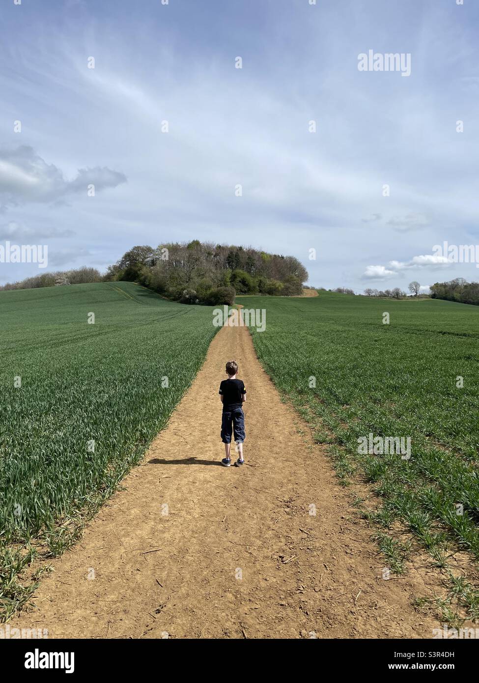 Disappearing perspective, boy on path through field on hill. - Smartphone Captured Stock Image