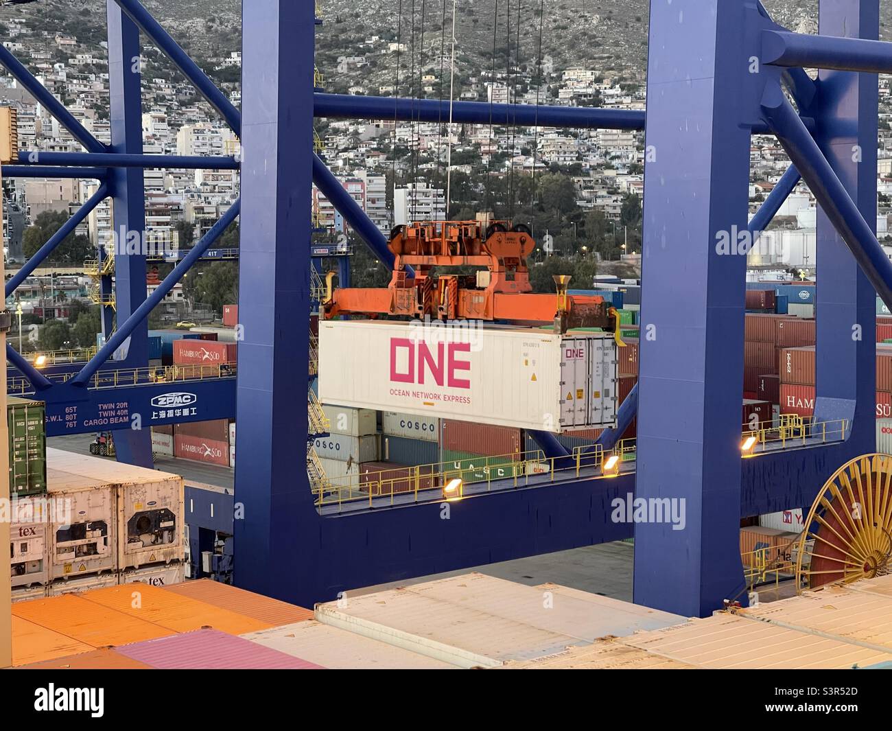 https://c8.alamy.com/comp/S3R52D/white-container-with-big-pink-letters-one-ocean-network-express-hanging-on-spreader-of-blue-gantry-cranes-in-container-terminal-in-port-of-piraeus-greece-in-background-are-family-houses-S3R52D.jpg