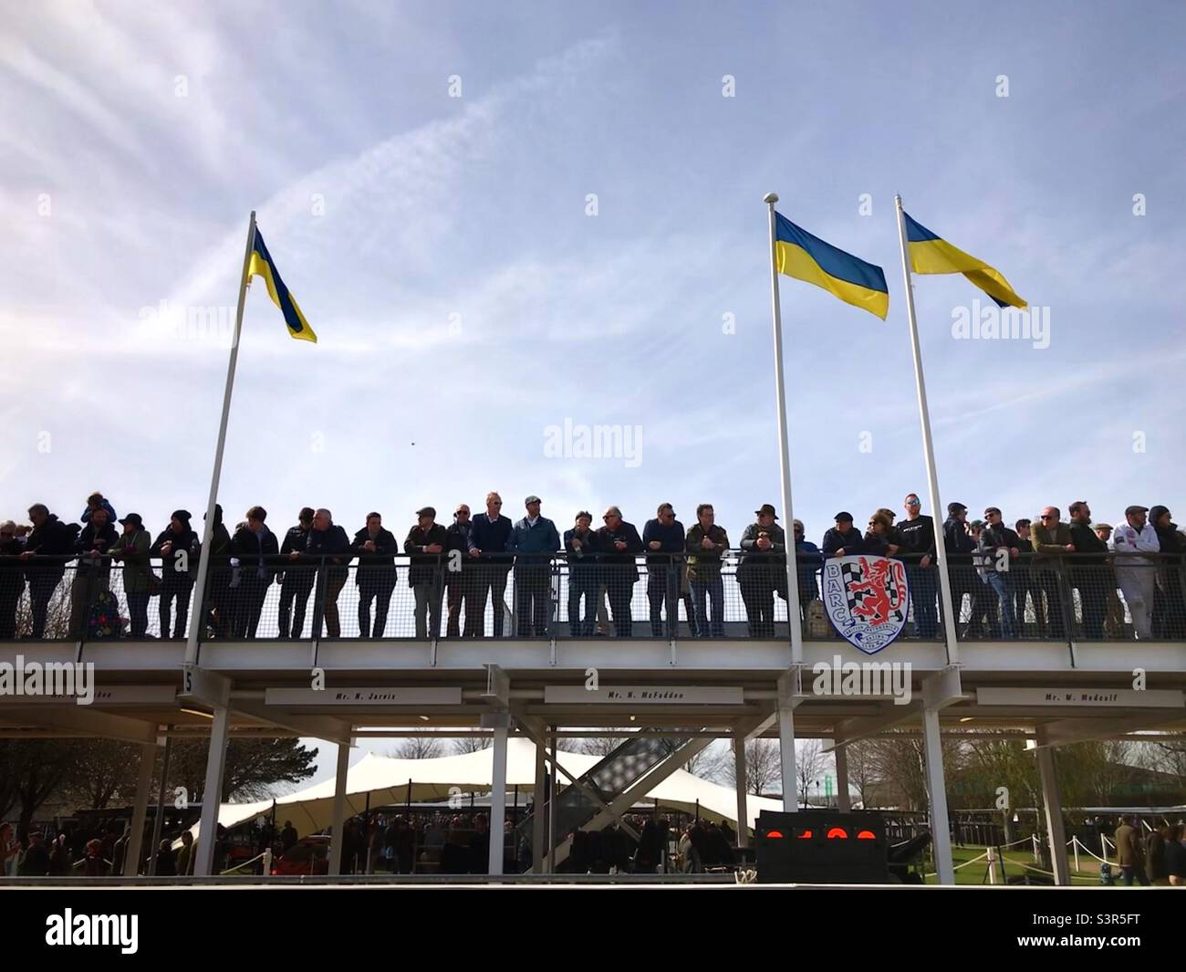 Goodwood stands with Ukraine, spectators standing above the pits at the 79th Members’ Meeting with Ukrainian flags flying. - Smartphone Captured Stock Image