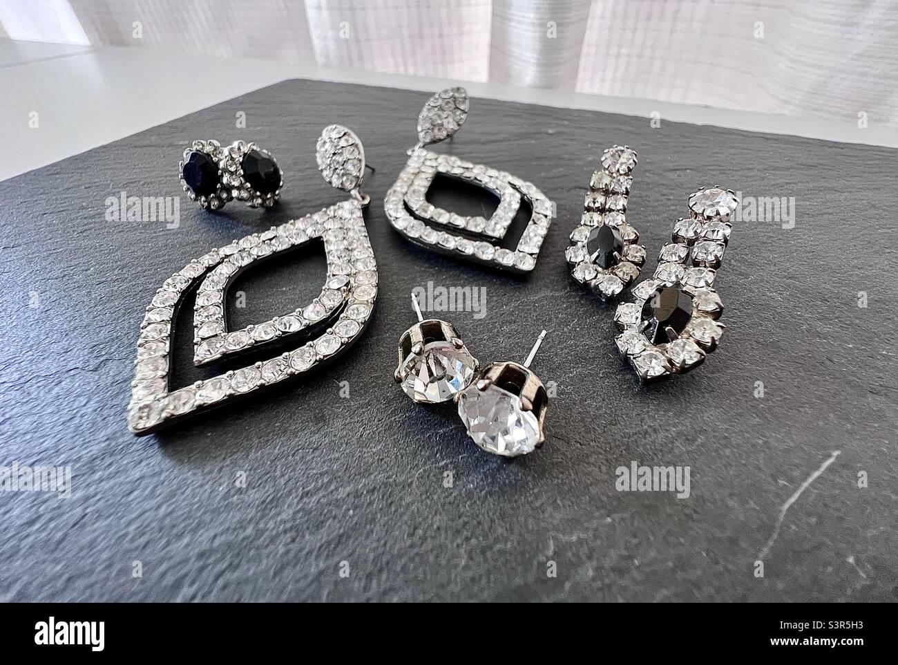 Still life photography display of vintage costume jewelry, earrings, clear  rhinestone and black gem on gray slate with white background Stock Photo -  Alamy