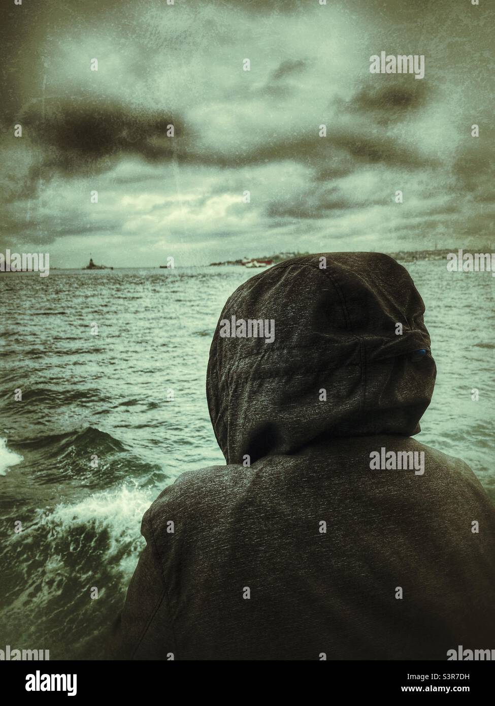 14 year old boy with hoodie looking to Bosphore sea from a ferry boat in a rainy  cloudy day Istanbul Turkey - Smartphone Captured Stock Image