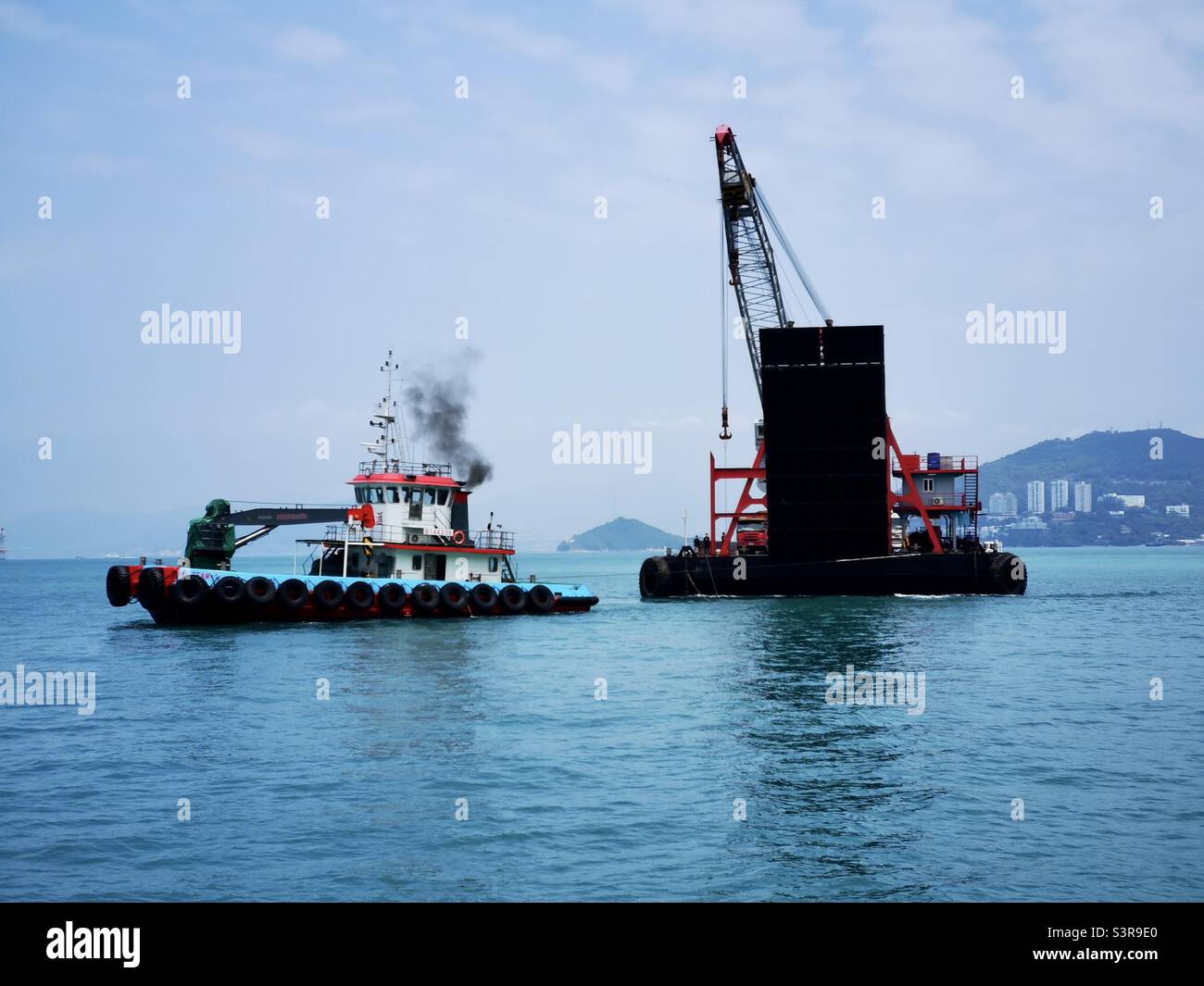 A barge pulling a crane and trucks for the construction of the new pier in Pak Kok, Lamma island,Hong Kong. Stock Photo