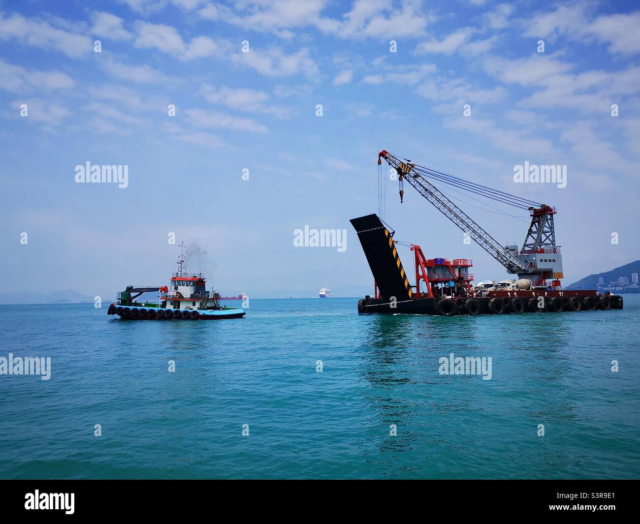 A barge pulling a crane and trucks for the construction of the new pier in Pak Kok, Lamma island,Hong Kong. - Smartphone Captured Stock Image