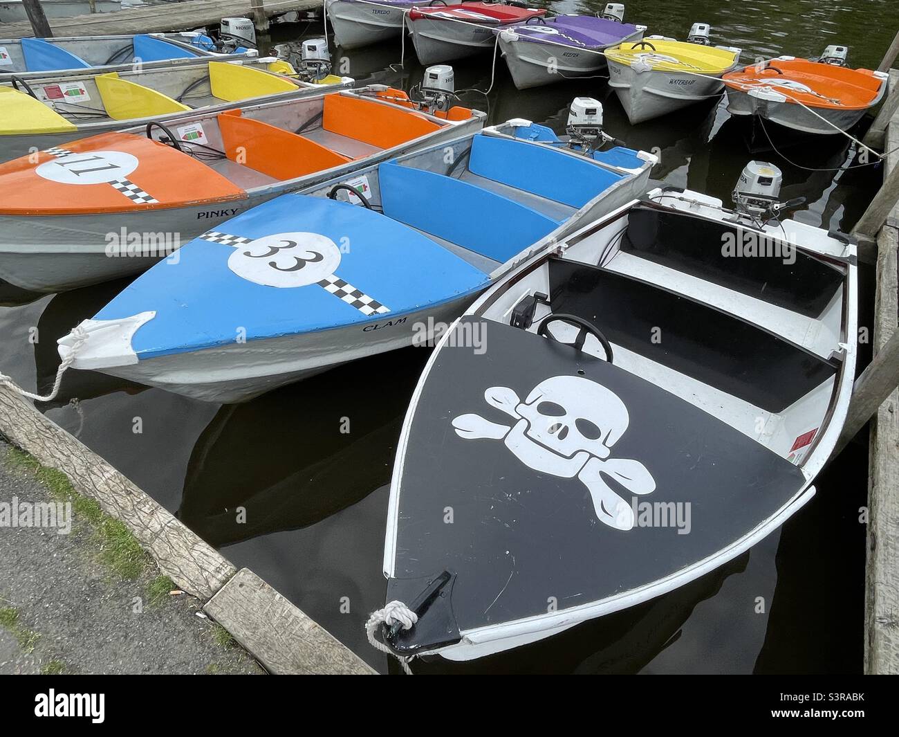 Small outboard motor boats for hire on the quayside at Henley on Thames, the foreground boat bearing a skull and crossbones motif - Smartphone Captured Stock Image
