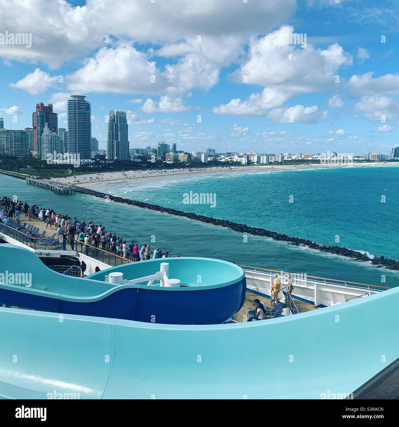 March, 2022, View of the beach and city from behind a water slide during the Sailaway Party as the Carnival Conquest cruise ship leaves Miami, Florida for a Bahamas cruise - Smartphone Captured Stock Image