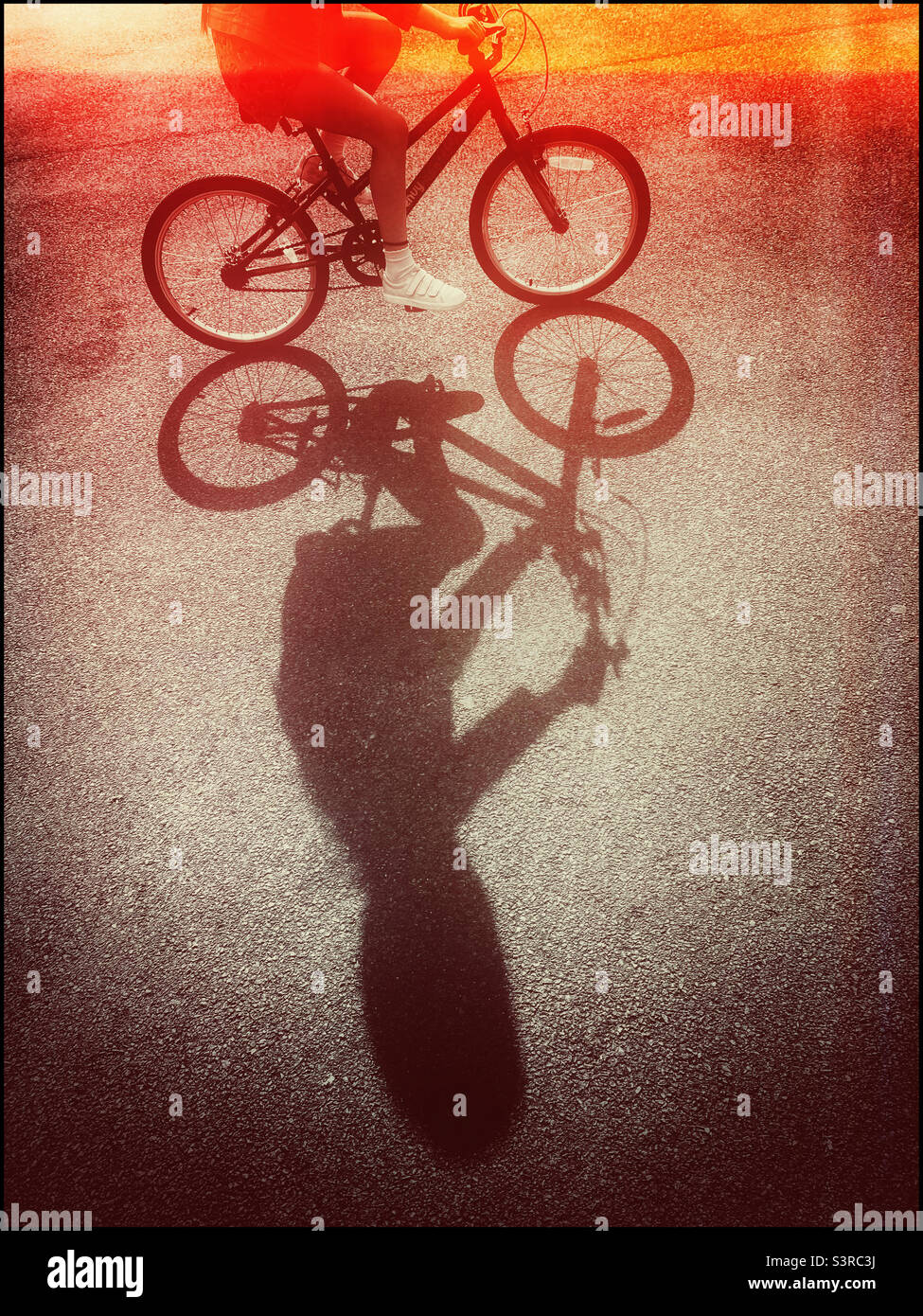 A retro film effect image of a girl riding her bicycle in the late afternoon sunshine. An interesting shadow? Photo ©️ COLIN HOSKINS. Stock Photo