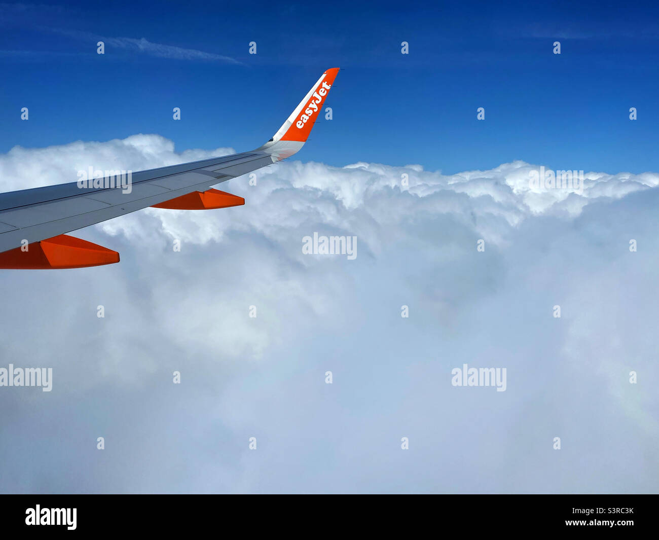 The wing of an easyJet A320 aircraft above the clouds, taking people to an exciting holiday destination. EasyJet is one of Europe’s largest budget airlines. Photo ©️ COLIN HOSKINS. Stock Photo